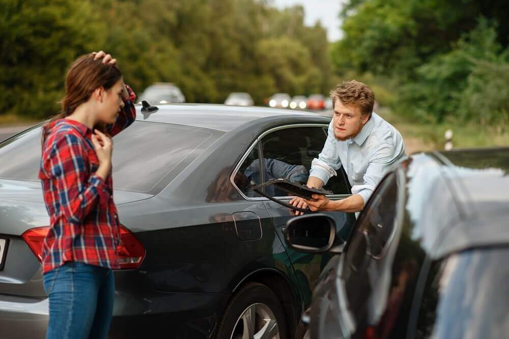 Driver complaining to uninsured female driver in car accident.